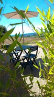 Un área de estar al aire libre con mesa y sillas, una sombrilla y vistas del paisaje.