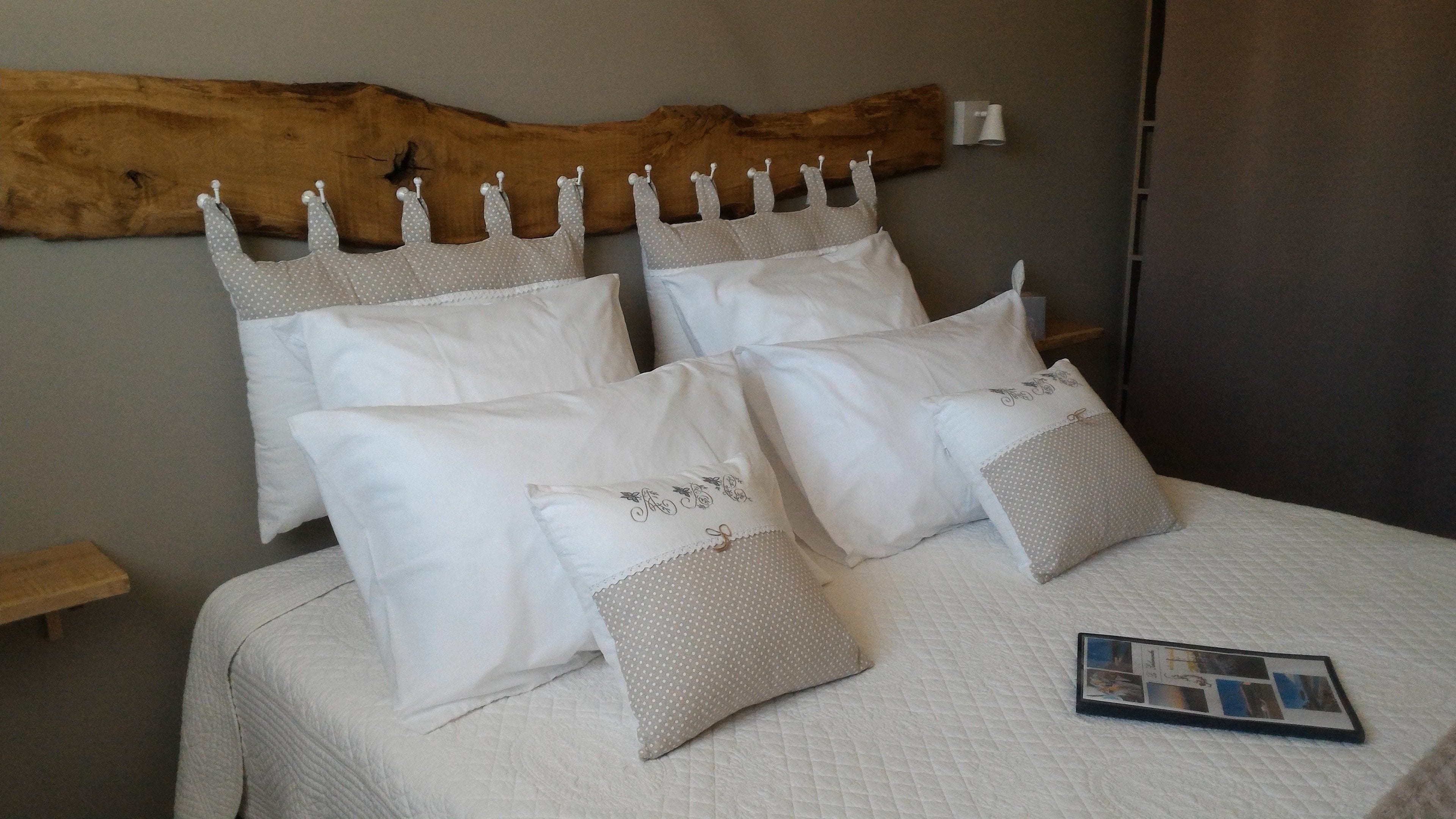 A bed with white bedding and multiple pillows, a wooden headboard, and a bedside table with a magazine.