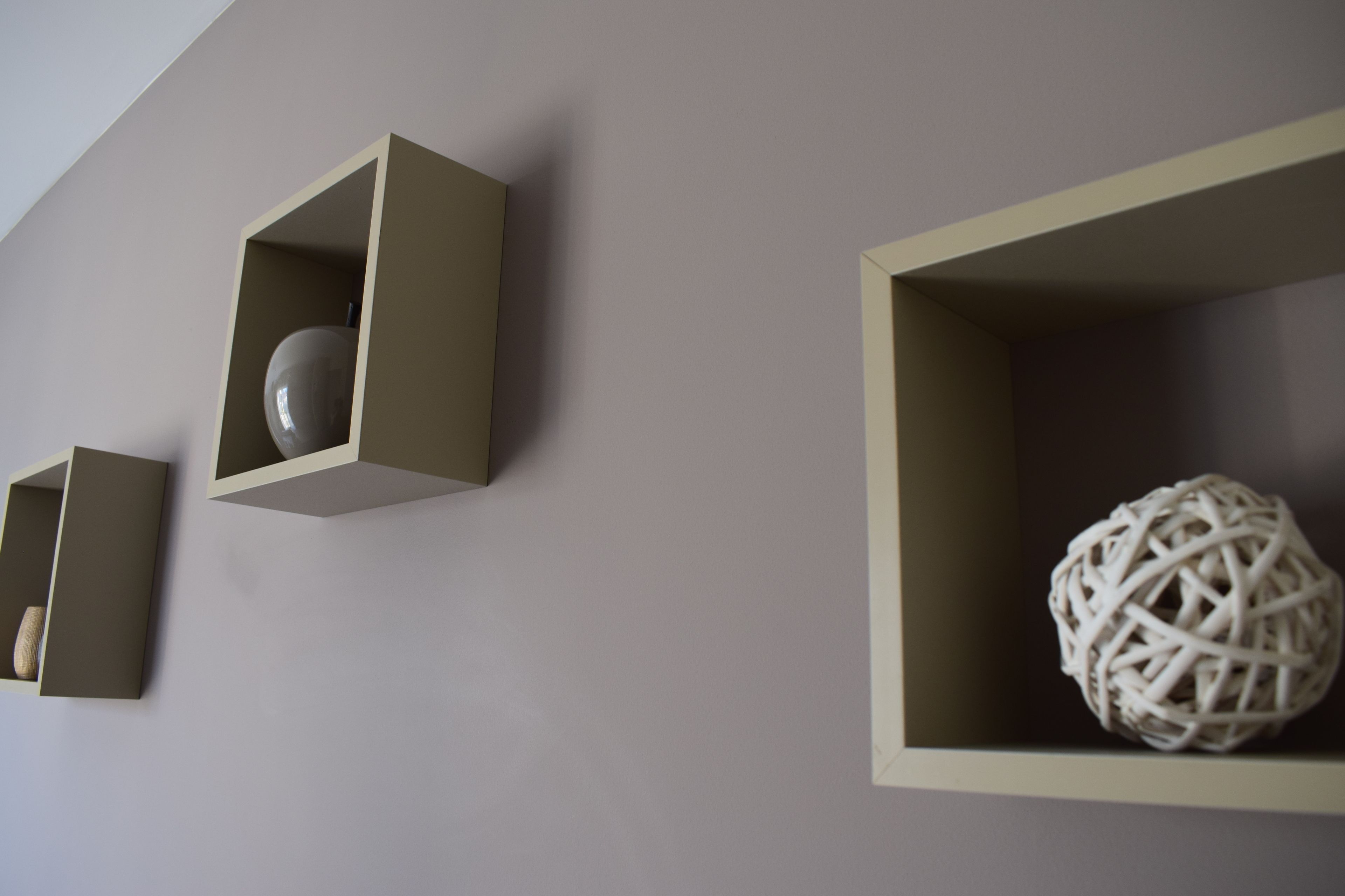 Three minimalist wall-mounted shelves with geometric shapes containing decorative items.