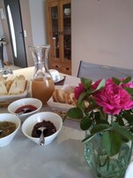 Una mesa con pan, mermelada, una jarrón de té y un florero con flores.