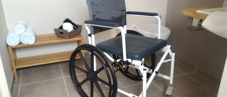 Un fauteuil roulant dans une salle de bain avec un banc en bois et des serviettes enroulées.