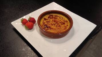 Eine Schale Crème brûlée auf einem weißen Teller, daneben drei Erdbeeren.