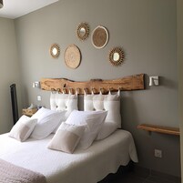 Un dormitorio con una cama grande, varias almohadas, cabecera de madera, luces fijadas en la pared y una estantería.