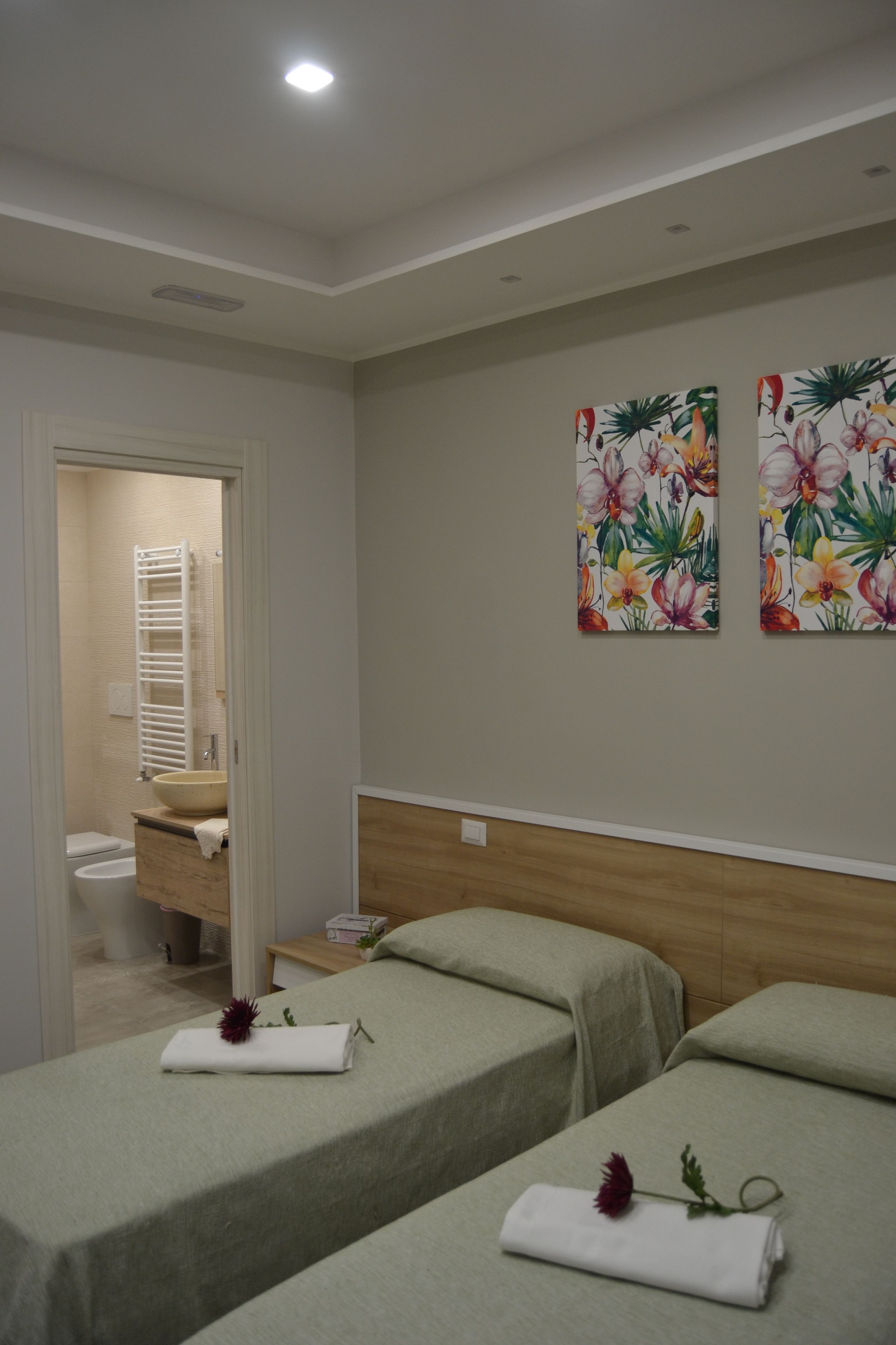 Habitación de hotel con dos camas, un baño con lavamanos y toallero, y decoración floral en las paredes.
