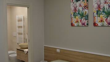 Quarto de hotel com duas camas, banheiro com pia e porta-toalhas, e arte floral na parede.