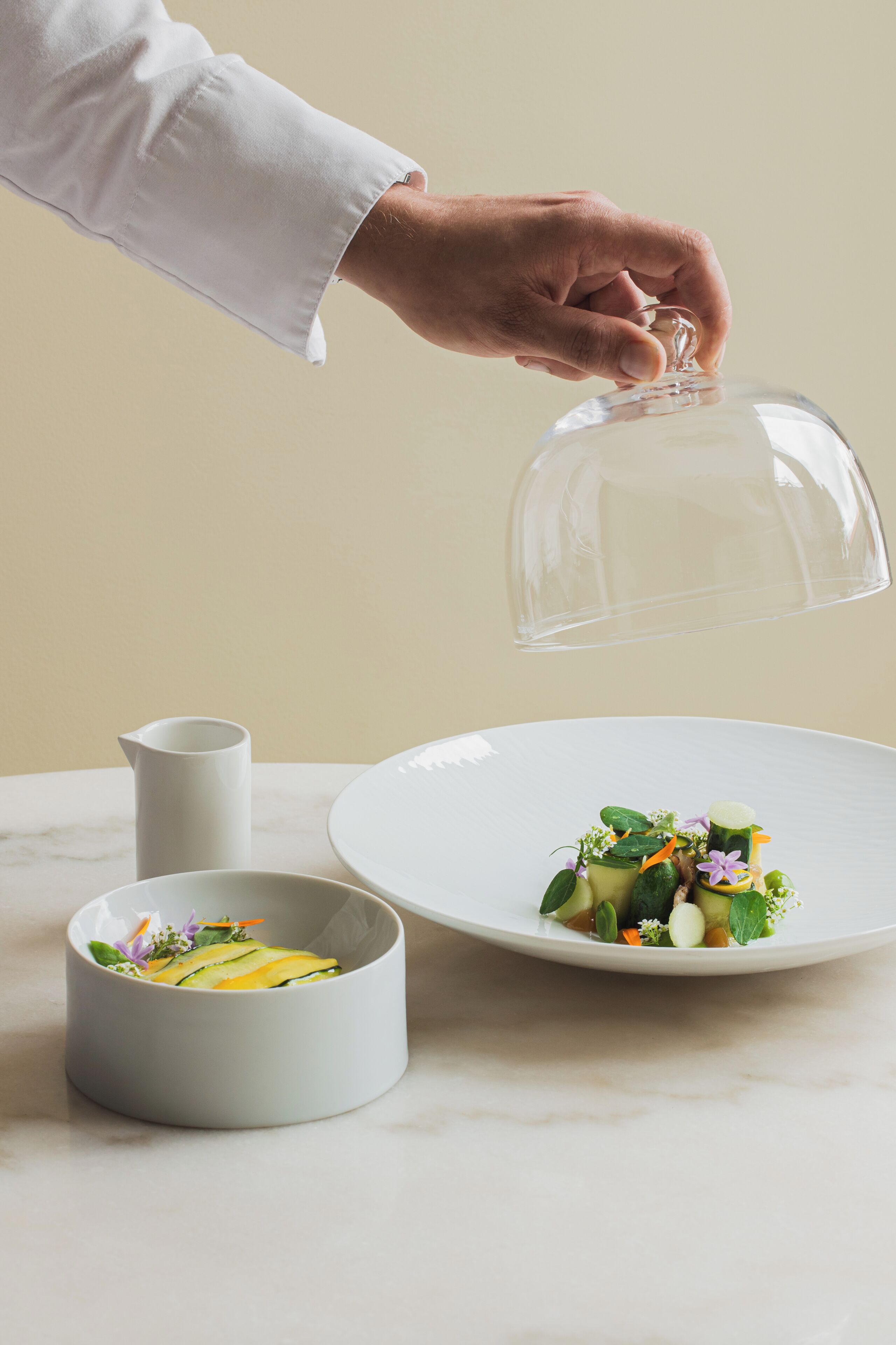 A hand holding a transparent dome over a plate of food.