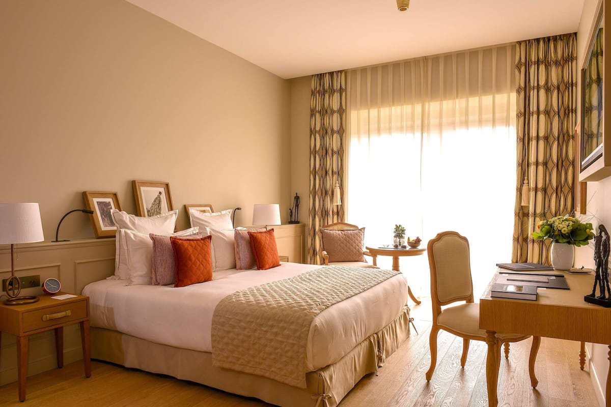 A hotel room with a large bed, bedside tables, a desk with a chair, and a window with curtains.