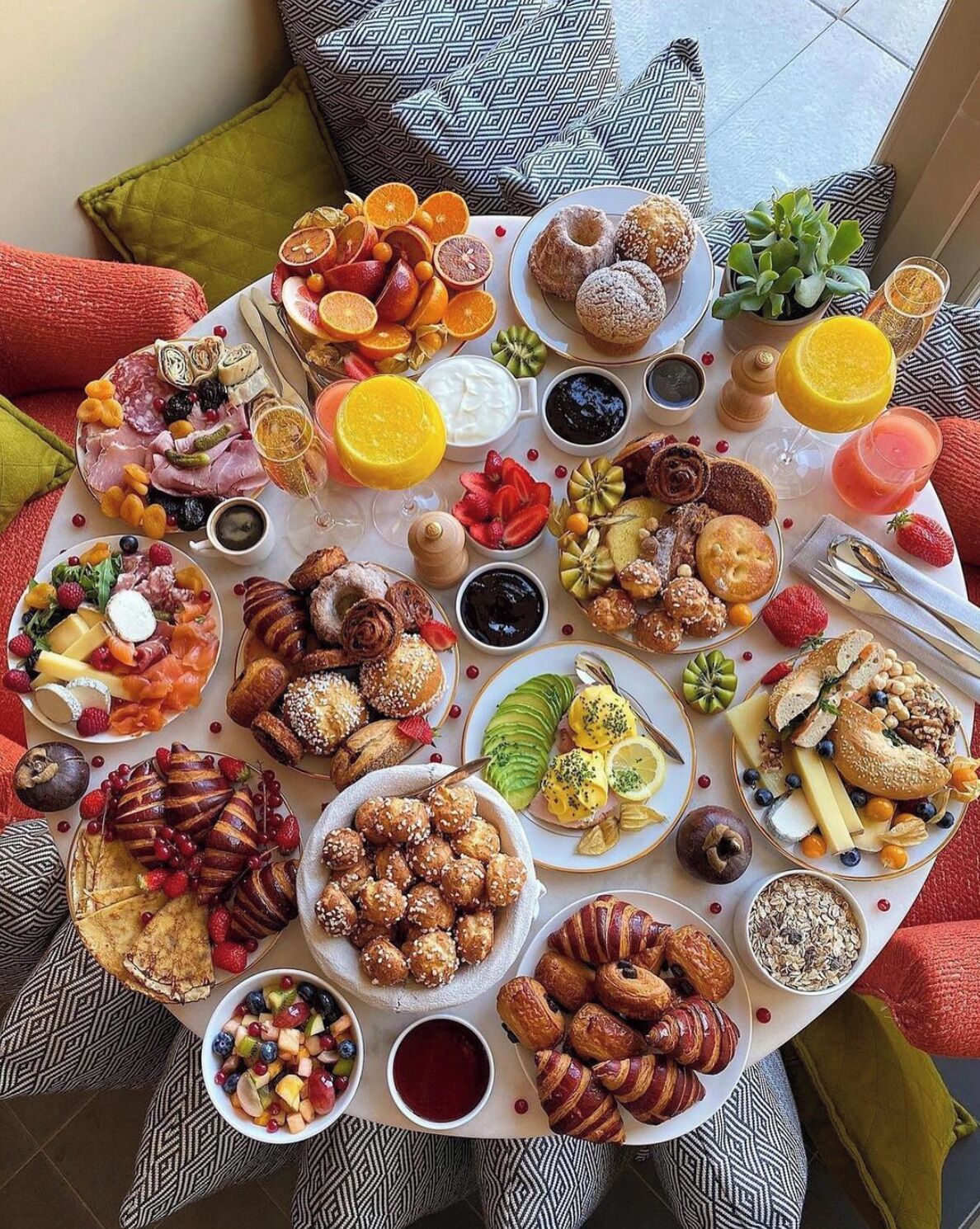 Una mesa redonda con diversas comidas y bebidas, rodeada de cojines estampados.