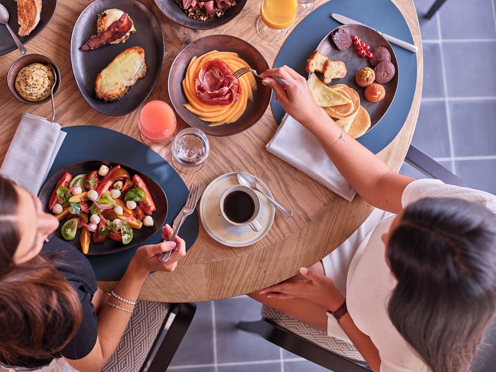 A round dining table with various breakfast dishes, a glass of orange juice, and a cup of coffee.