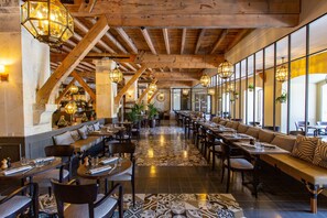 A spacious restaurant with high wooden ceilings, multiple seating areas, and hanging light fixtures.
