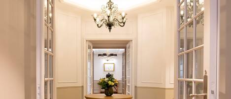 A hallway with a patterned floor, a central table with a vase, and a chandelier.