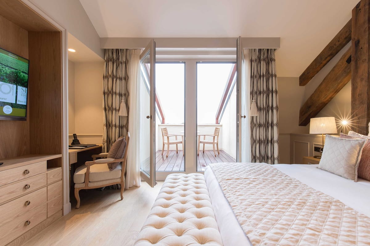 A hotel room with a large bed, a desk, a chair, and a balcony with a view.