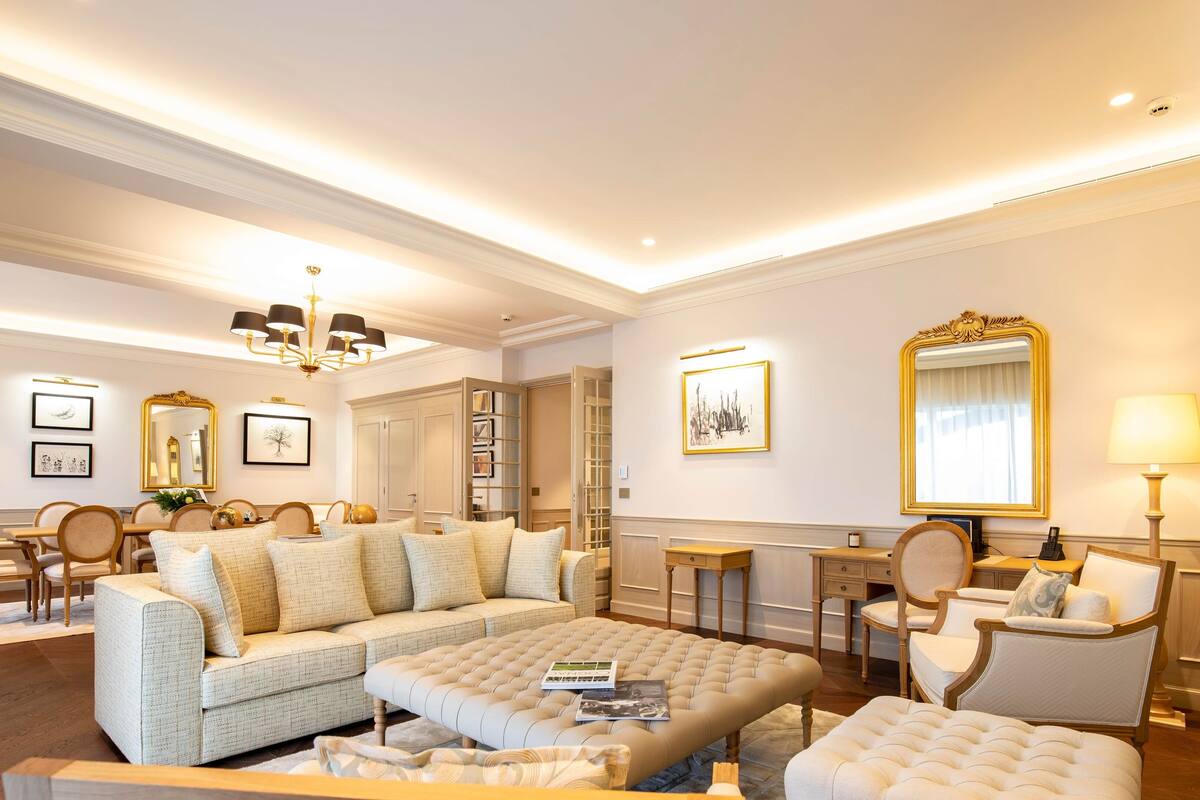 A spacious living room with a large sectional sofa, a tufted ottoman, and a dining area with a wooden table and chairs.