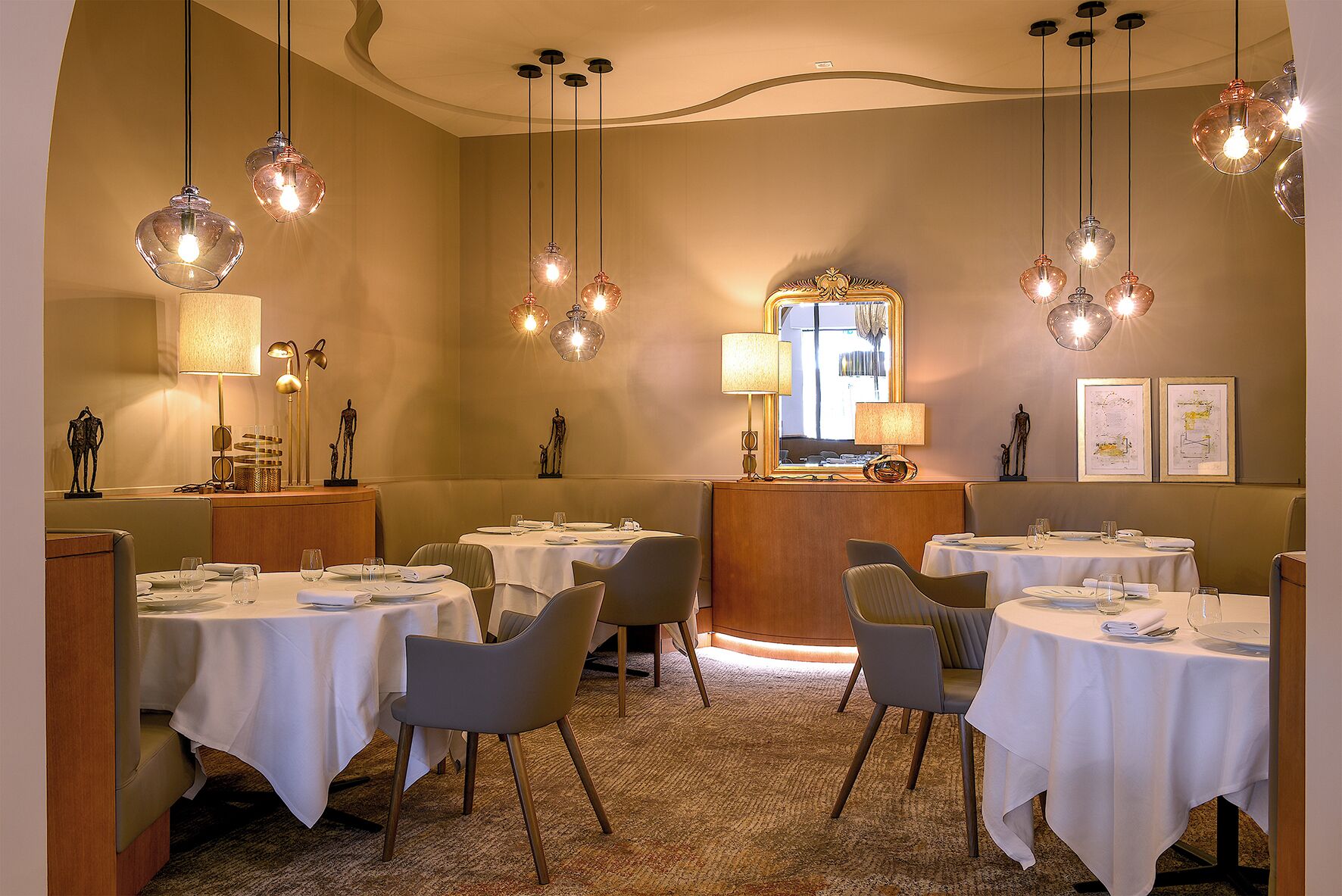 Un comedor con mesas redondas, sillas, lámparas colgantes y un espejo.