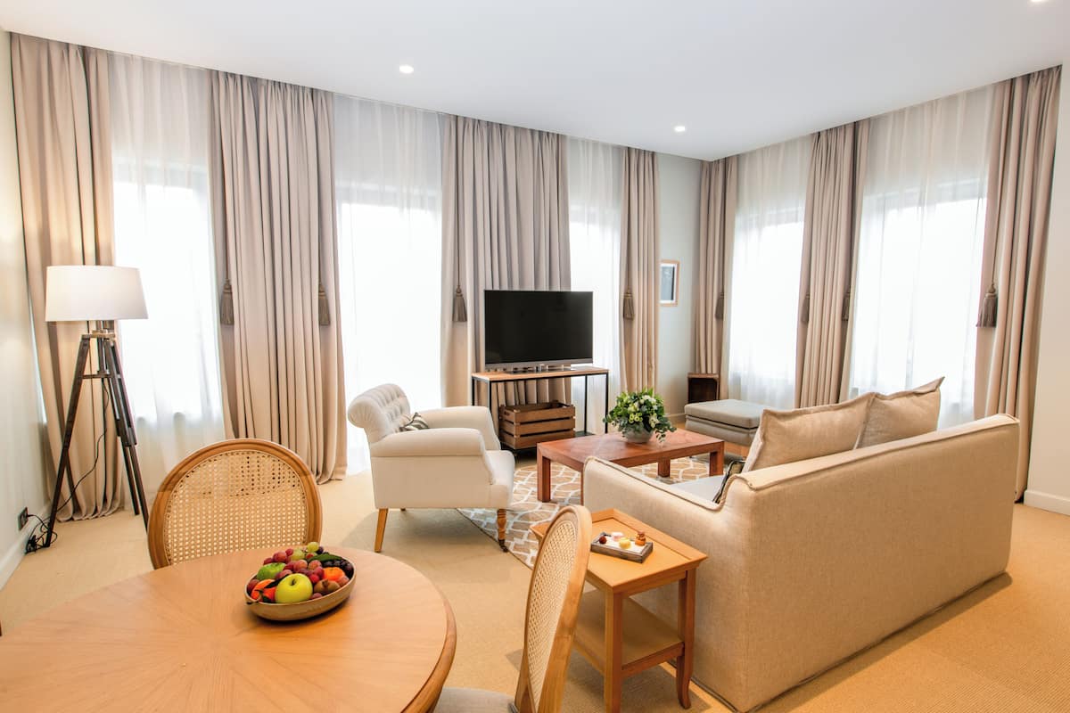 A modern living room with a sofa, a dining table with fruit, a TV, and curtains.