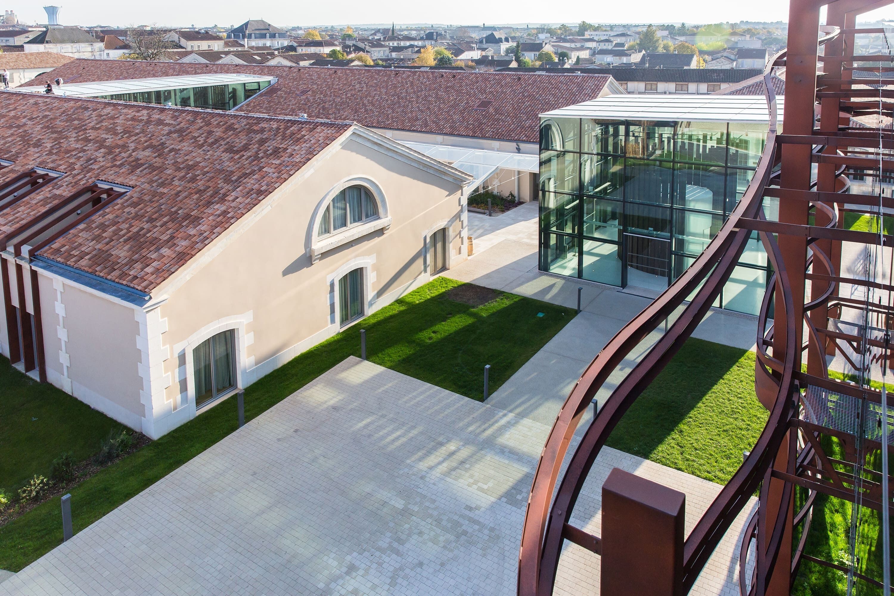 A modern building with a glass facade, a courtyard with a green lawn, and a traditional building with a tiled roof.
