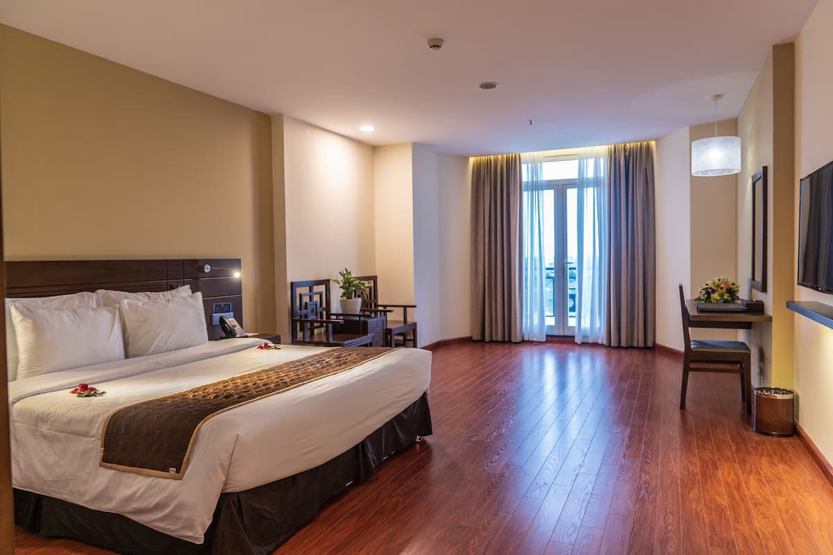Une chambre d’hôtel avec un grand lit, un bureau, une chaise, une télévision et une fenêtre avec des rideaux.