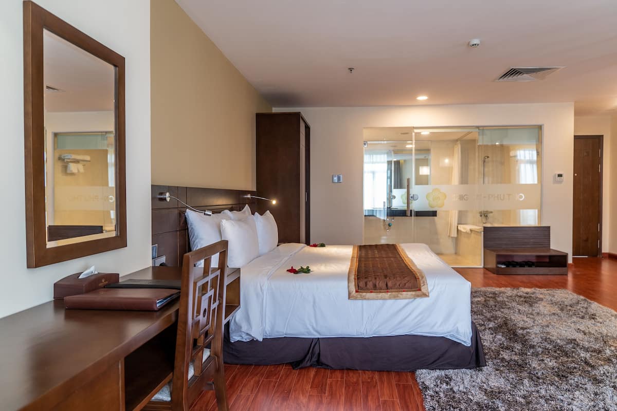 Une chambre d’hôtel avec un grand lit, un bureau en bois, une chaise, un miroir et une vue sur la salle de bain.