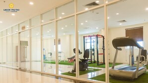 Ett gym med träningsutrustning, inklusive löpband och styrketräningsmaskiner, och en glasvägg som skiljer gymmet från korridoren.