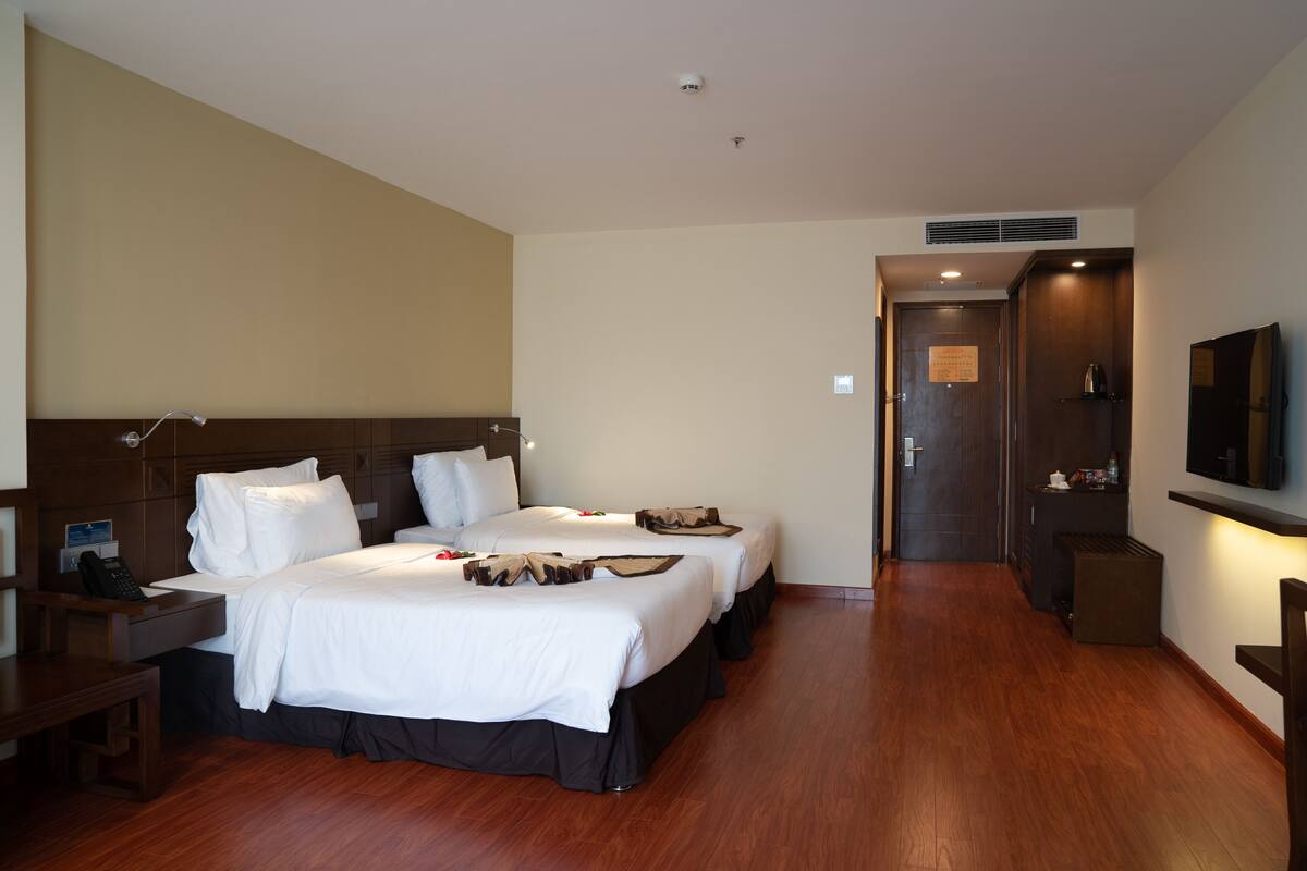 Une chambre d’hôtel avec deux lits, un bureau, une chaise, une télévision et une porte donnant sur une salle de bain.