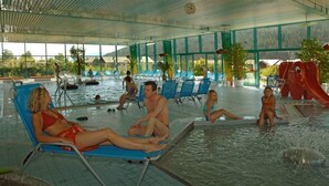 An indoor swimming pool with lounge chairs, a slide, and a view of the outdoors. - Meine Heimat (Ramsau am Dachstein)