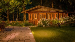 A wooden cabin with large windows, surrounded by a garden with white flowers and a paved pathway. - Meine Heimat (Ramsau am Dachstein)