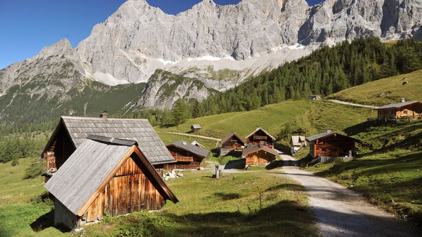 A mountain village with wooden houses, a dirt path, and a backdrop of rocky mountains. - Meine Heimat (Ramsau am Dachstein)