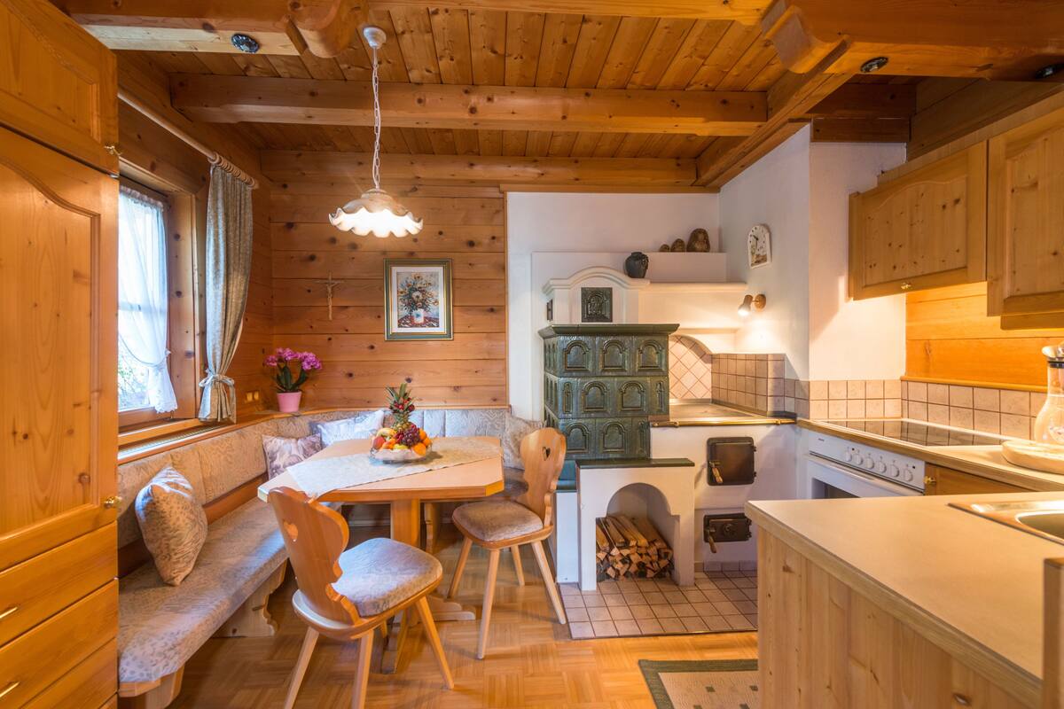 Interior acolhedor de uma cabana com paredes de madeira, área de jantar com banco, cozinha com fogão e luminária pendente.