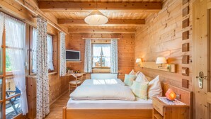 A wooden cabin bedroom with a bed, bedside table, lamp, and a TV on the wall. - Meine Heimat (Ramsau am Dachstein)