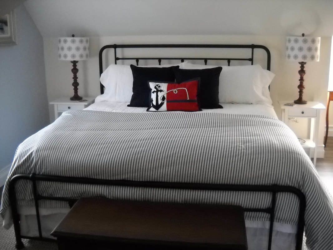A neatly made bed with a striped bedspread, two bedside tables with lamps, and a bench at the foot of the bed.