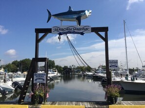 A marina entrance with a sign for Seaborn Marina Weigh Station, boats docked, and a large shark sculpture above. - The Ocean Bay House (Bay Shore)
