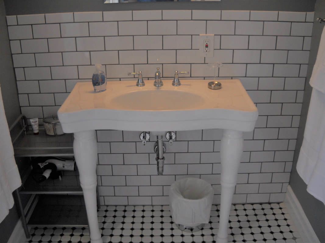 A bathroom with a white sink, three faucets, a soap dispenser, and a trash bin.