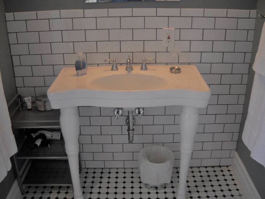 A bathroom with a white sink, three faucets, a soap dispenser, and a trash bin.