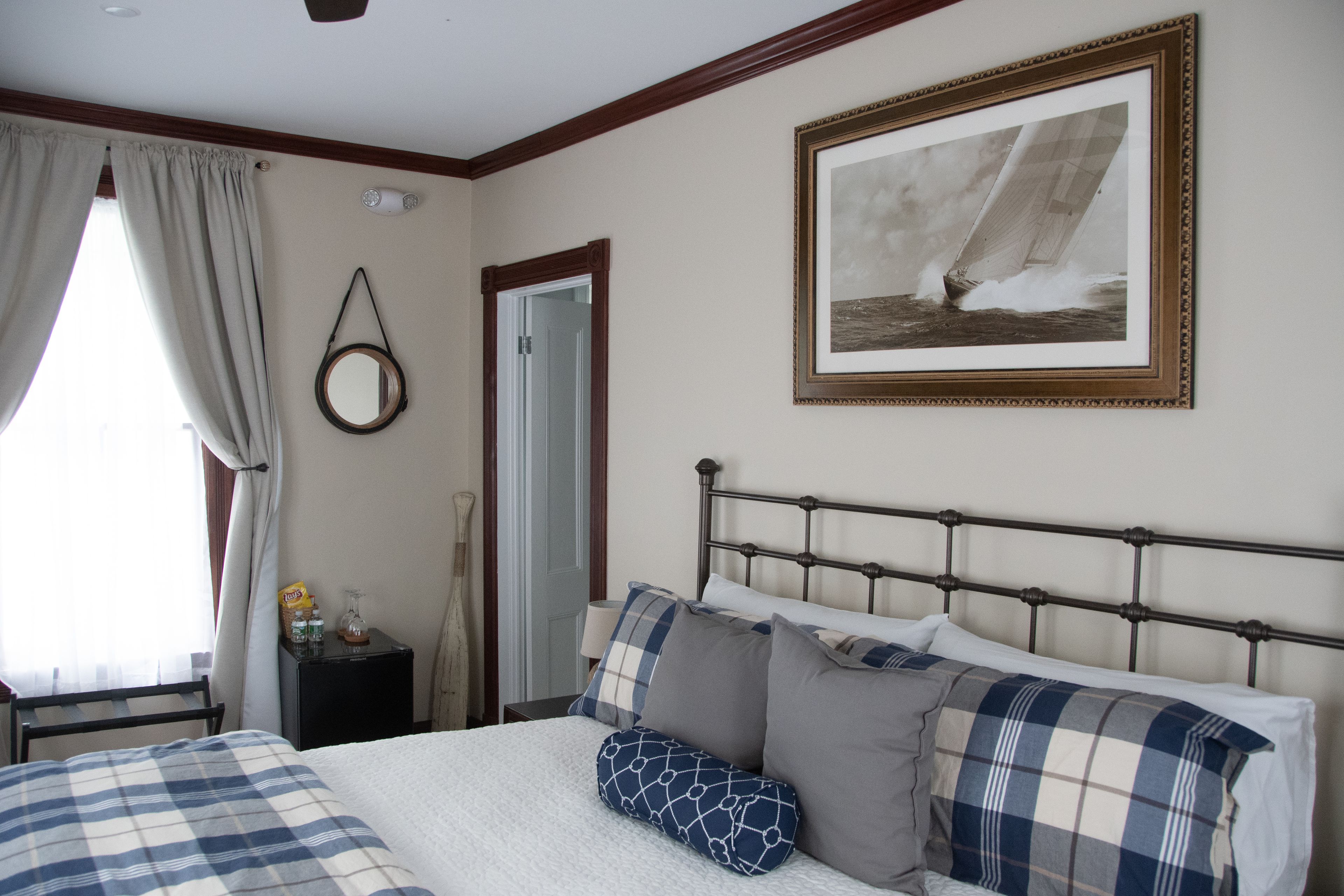 Un dormitorio con cama, una mesita de noche con lámpara, un cuadro enmarcado en la pared y una ventana con cortinas.