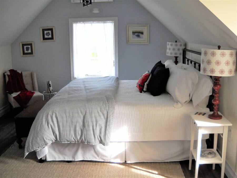 Ein Schlafzimmer mit einem großen Bett, einem Nachttisch mit Lampe, einem Sessel und einem Fenster.