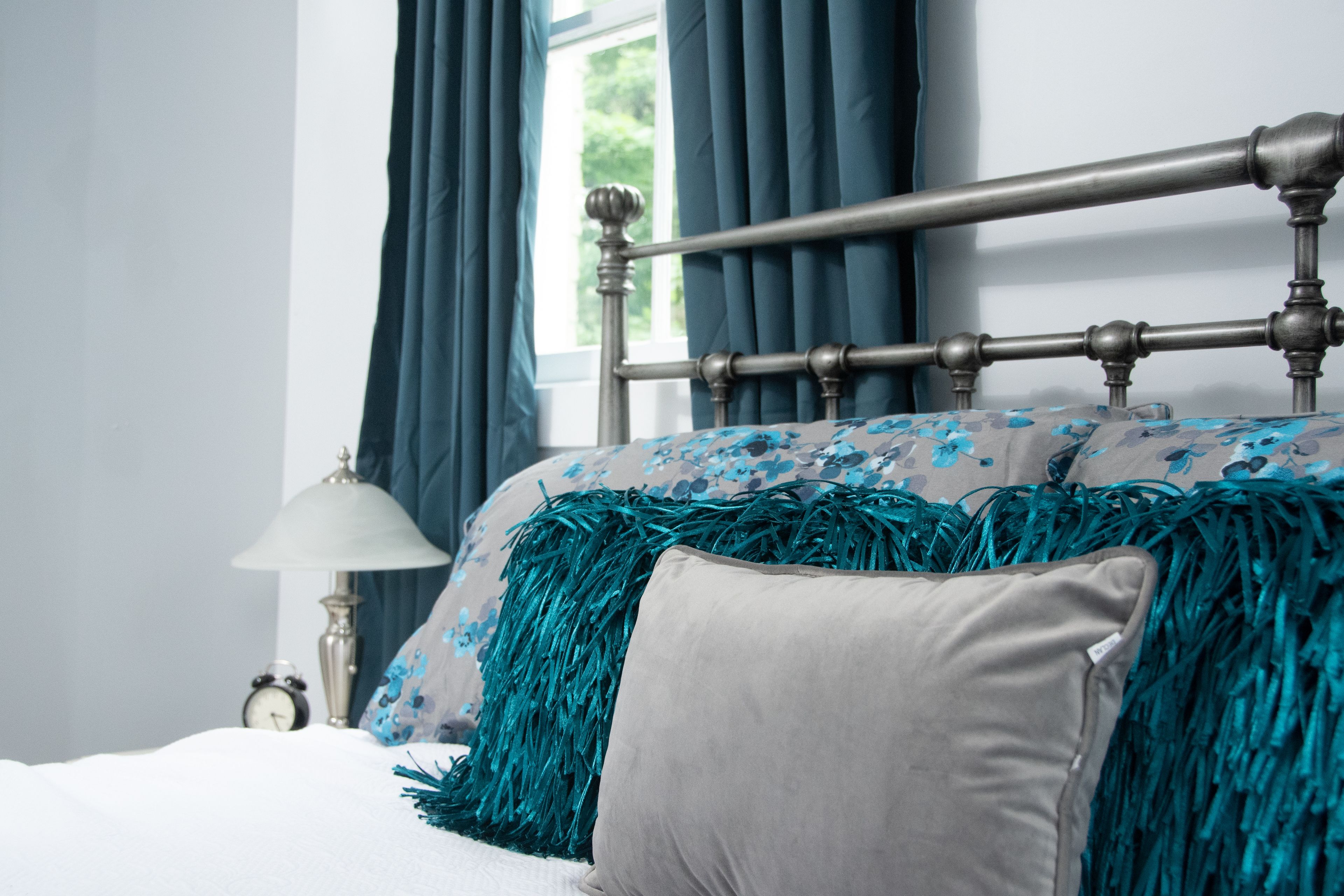 A neatly made bed with a headboard, a bedside lamp, and a window with curtains.