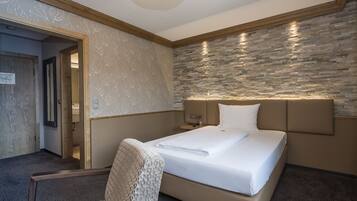 Une chambre d’hôtel avec un lit, une chaise, une table de chevet et un mur décoré d’un motif imitant la pierre.