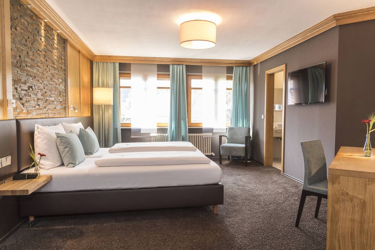 A modern hotel room with a large bed, a TV, a desk, and a chair.