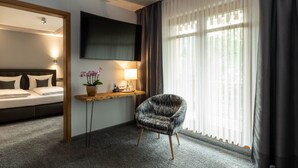 A hotel room with a bed, a TV mounted on the wall, a desk with a lamp, a chair, and a window with curtains. - Hotel & Restaurant Becher (Donzdorf)