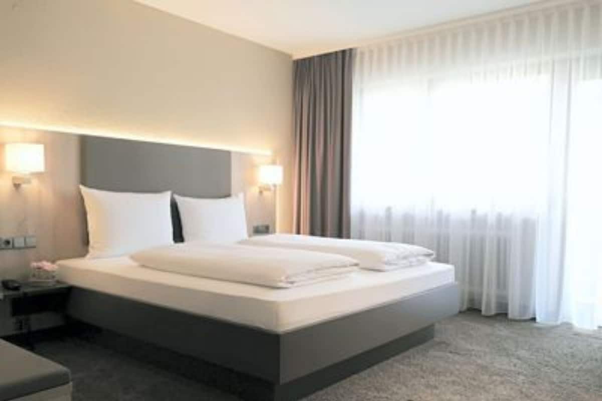 A modern hotel room with a large bed, two bedside tables, and a window with curtains.
