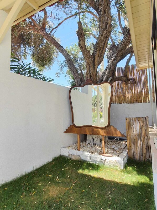 Un árbol en un patio trasero con una escultura de metal y una valla de bambú.