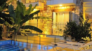 A hotel with a stone facade, balconies, and a pool area with lounge chairs. - Giritlim Butik Otel (Cesme)