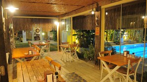An outdoor dining area with wooden tables and chairs, a thatched roof, and a view of a pool. - Giritlim Butik Otel (Cesme)