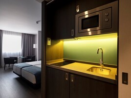 Una camera d'albergo compatta con angolo cottura, un letto, un tavolino e una sedia.