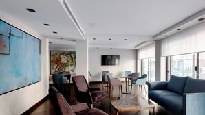 A spacious lounge with modern furniture, a large abstract painting, and a city view. - HG City Suites Barcelona (Barcelona)