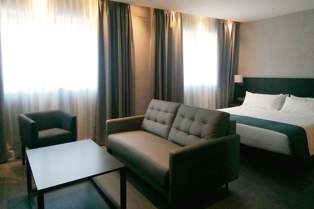 A hotel room with a bed, a sofa, a chair, and a small table.