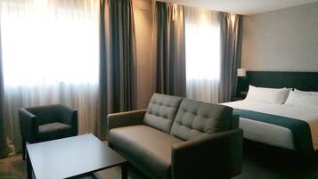 A hotel room with a bed, a sofa, a chair, and a small table.