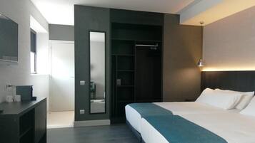 A modern hotel room with a large bed, a walk-in closet, a mirror, and a bedside table.