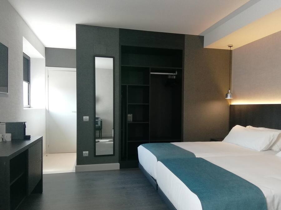A modern hotel room with a large bed, a walk-in closet, a mirror, and a bedside table.