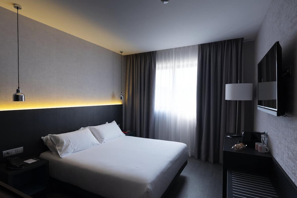 A hotel room with a large bed, bedside table, lamp, and a mirror.